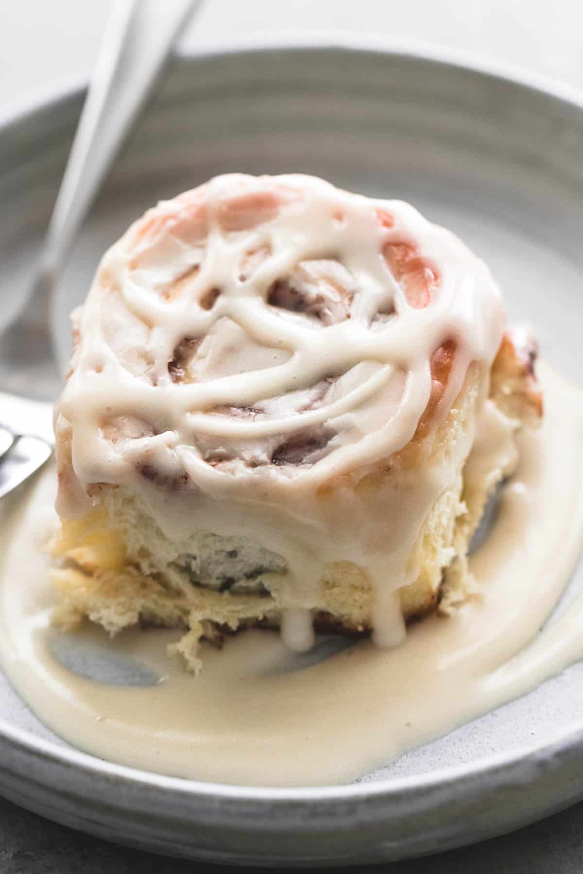 close up of a cream cheese cinnamon roll with a fork on a plate.