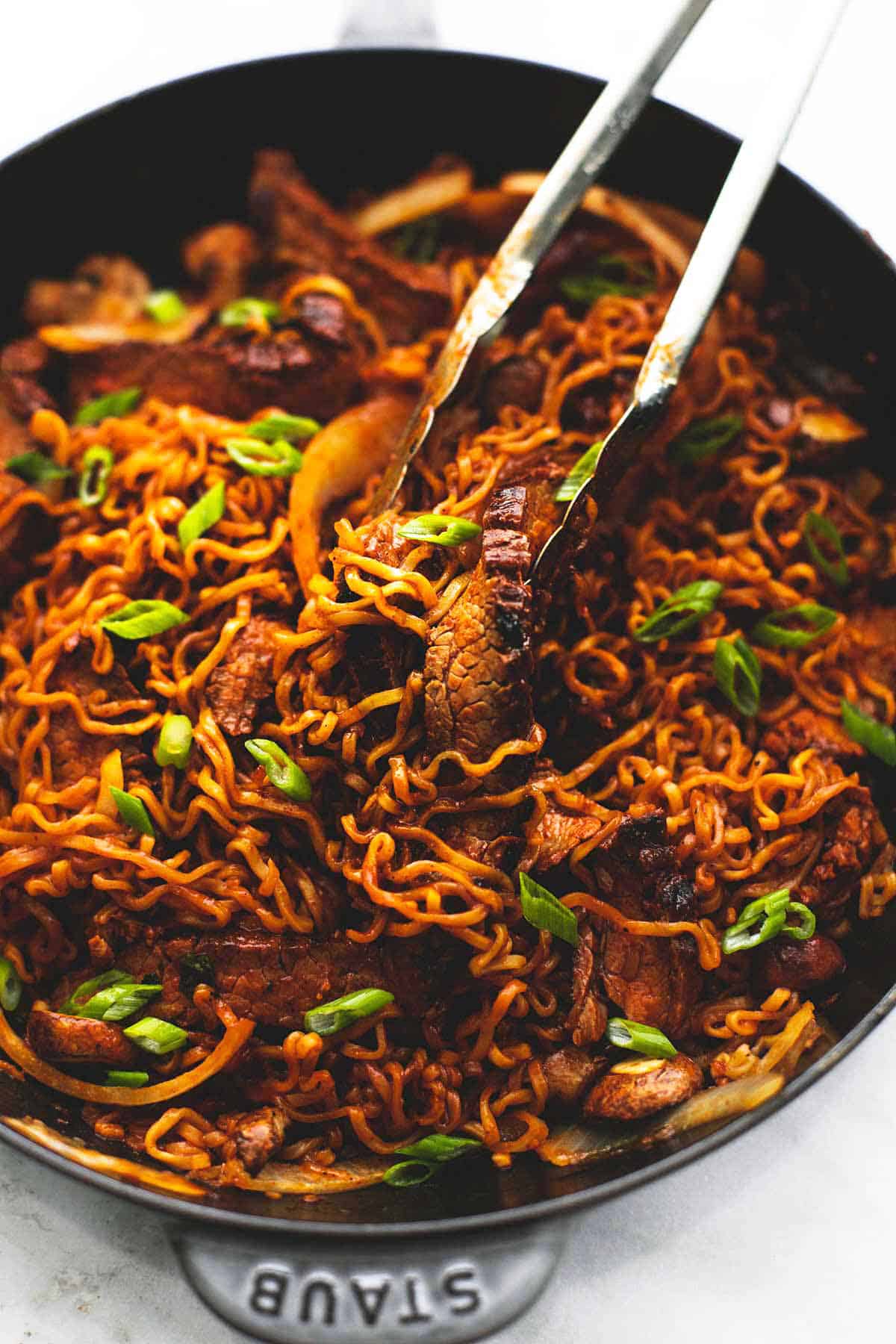 spicy Korean beef noodles with tongs in a skillet.