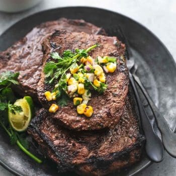 up close view of grilled steak with corn salsa on a black plate with forks