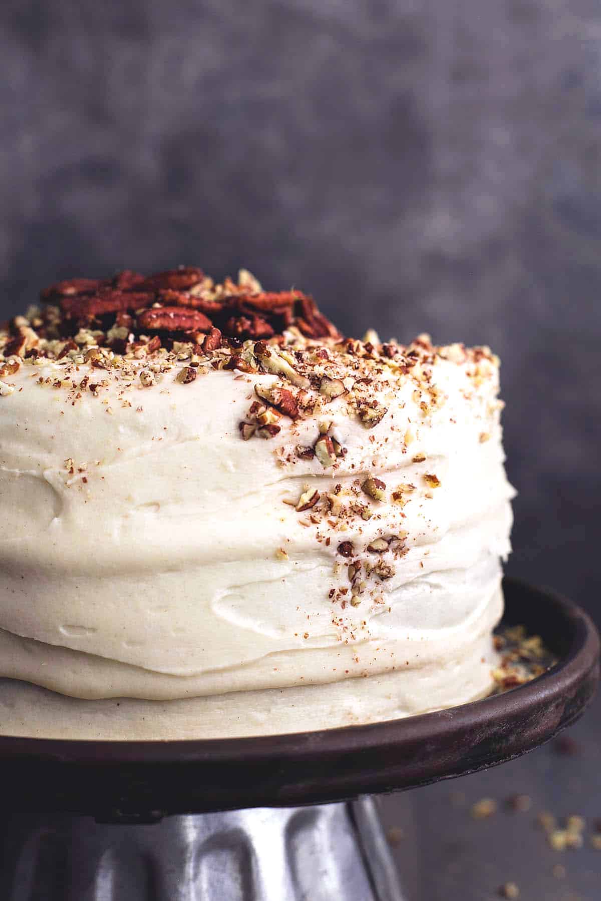 whole cake with white frosting and pecans on cake stand.