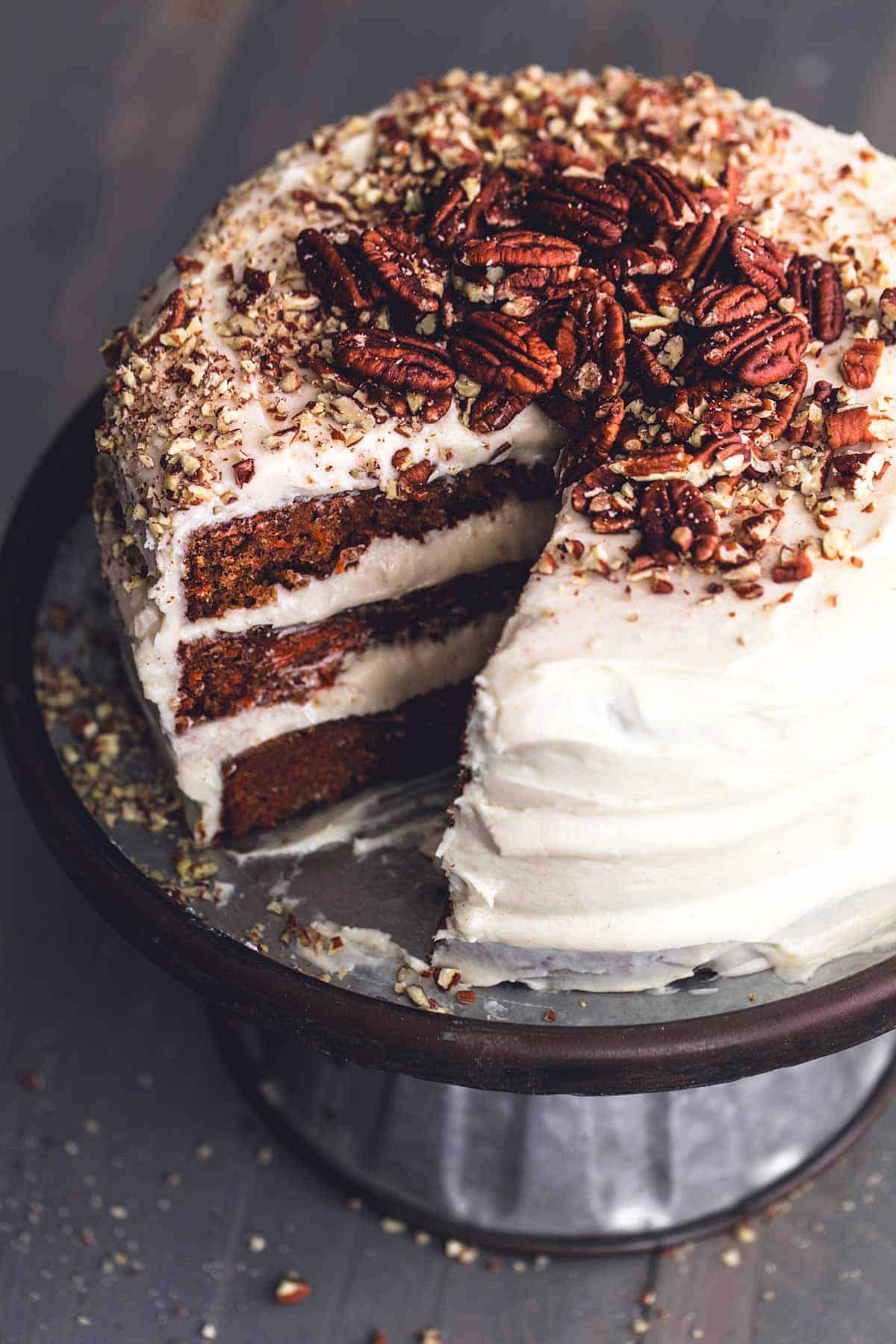 carrot cake with slice missing and pecans on top.