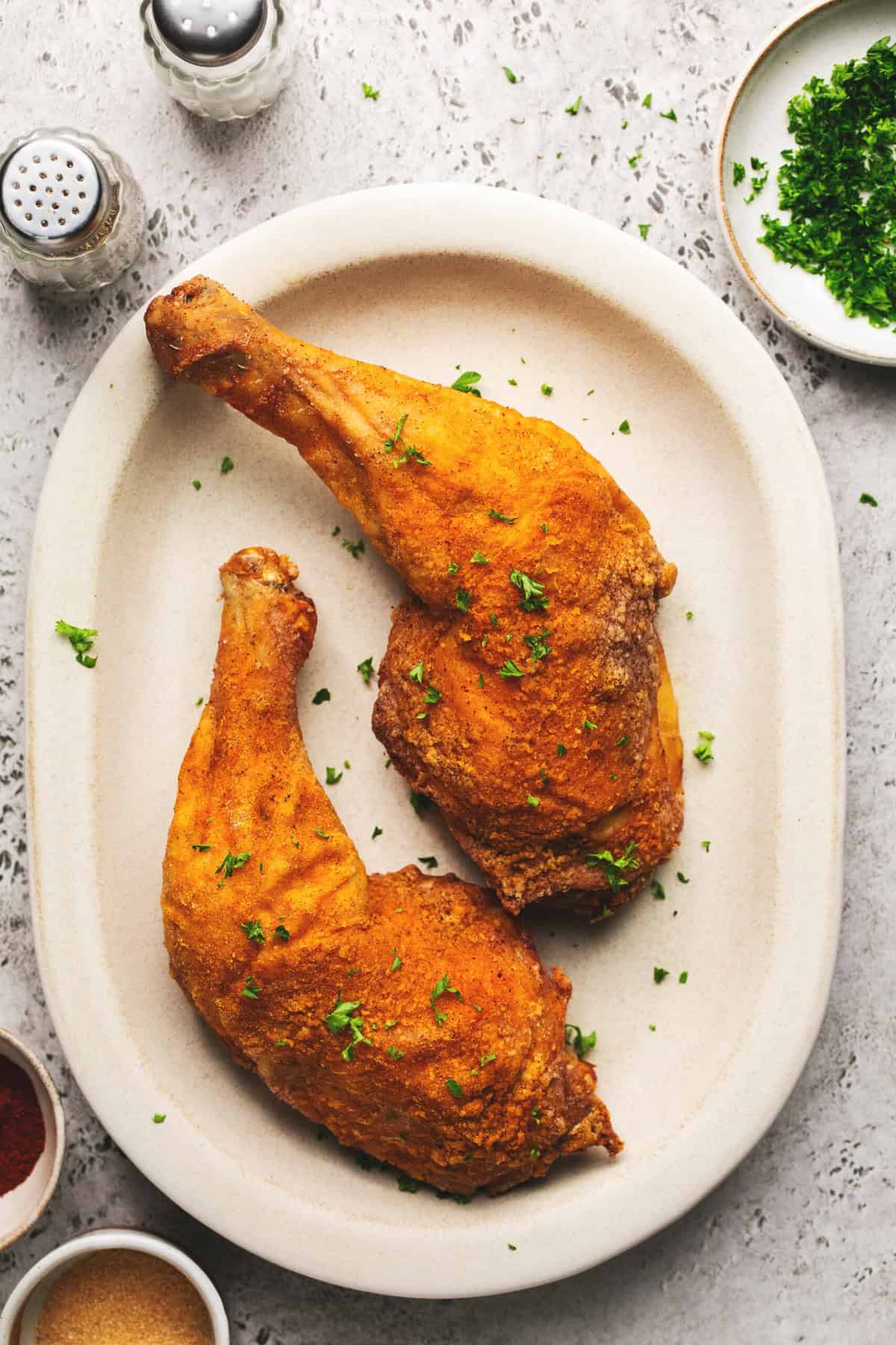 overhead view of air fryer chicken legs on platter with seasonings in pinch bowls