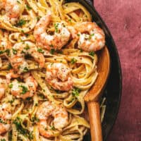 shrimp alfredo pasta in a skillet with wooden serving spoon