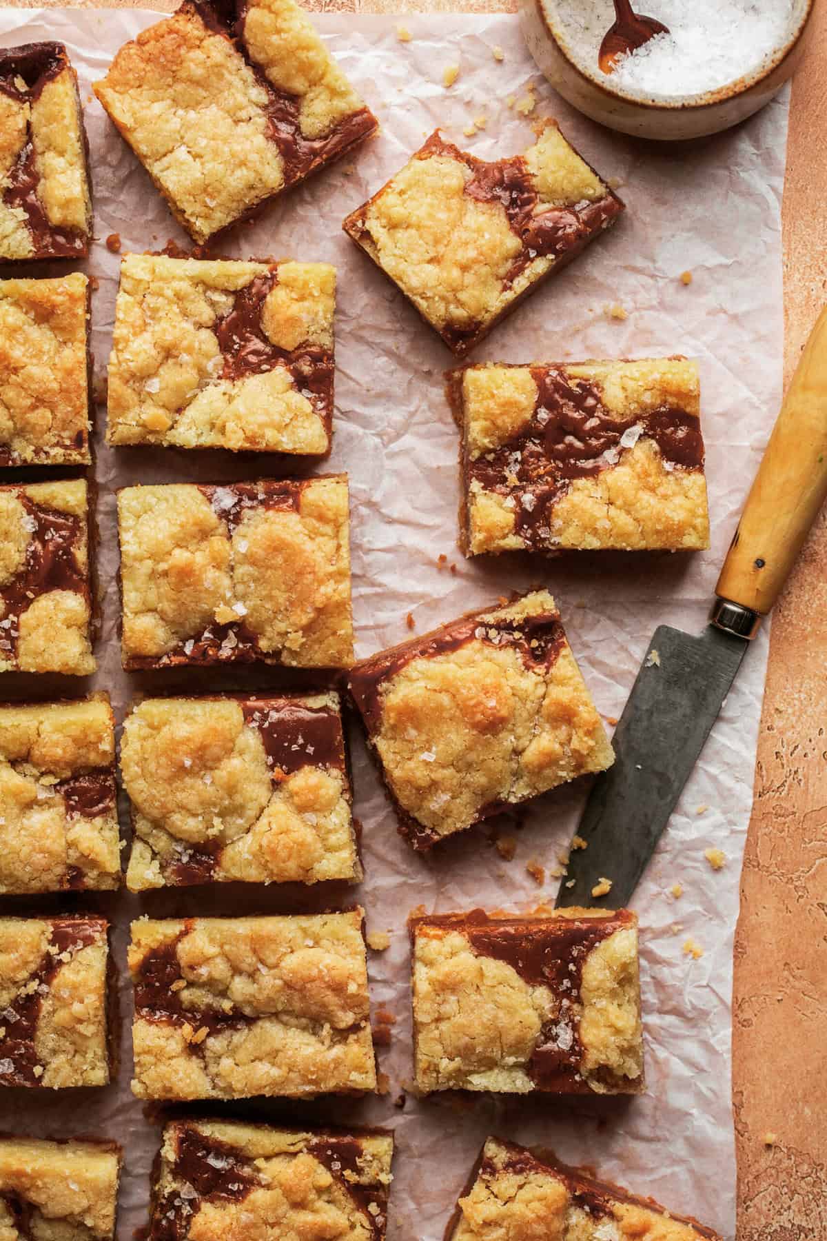 caramel cookie bars cut into squares on parchment paper with knife