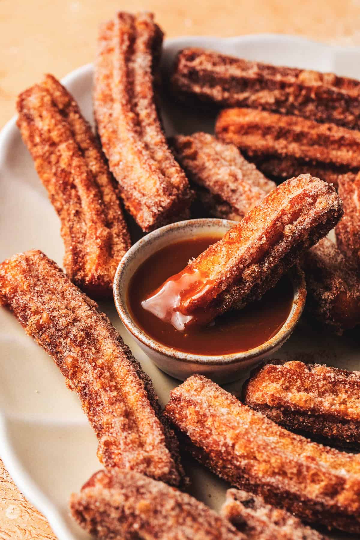 churro dipping into caramel sauce in bowl surrounded by more churros