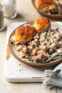 biscuits and sausage gravy in bowl with fork on cutting board