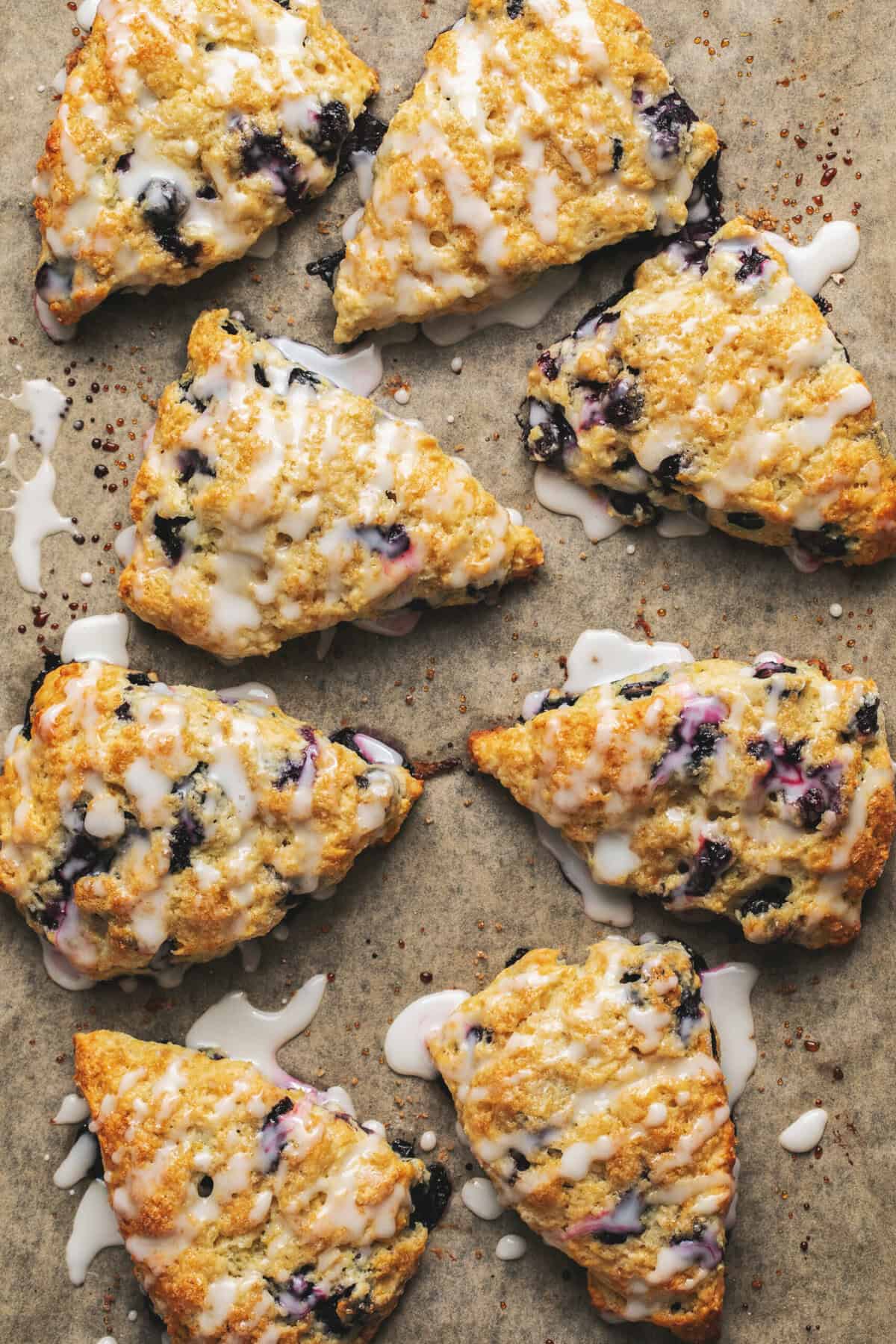 overhead view of blueberry scones with glaze on parchment