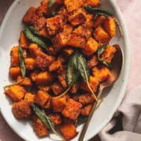 cubed and roasted butternut squash on serving dish with spoon and napkin