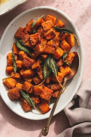 cubed and roasted butternut squash on serving dish with spoon and napkin