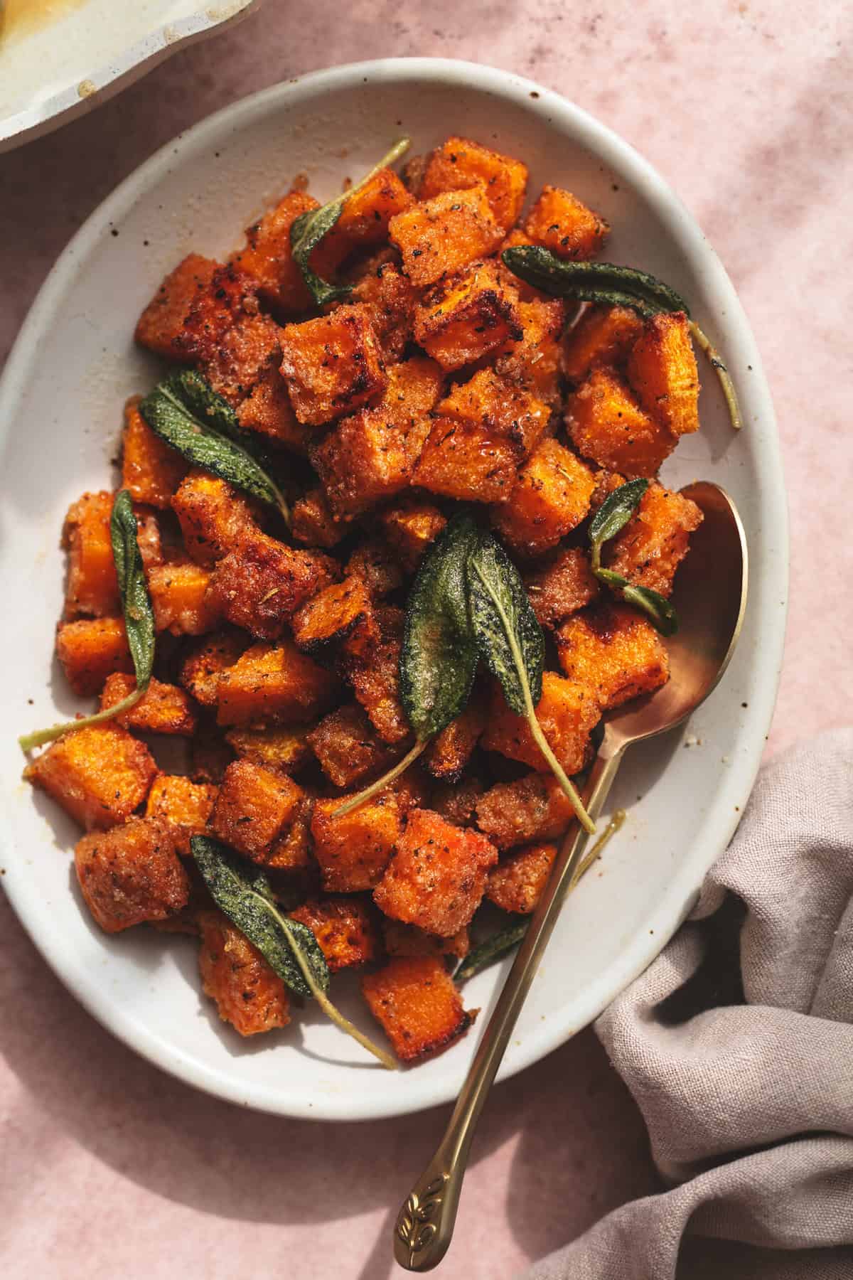 cubed and roasted butternut squash on serving dish with spoon and napkin