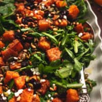 arugula salad on platter with roasted butternut squash, cranberries, and seeds