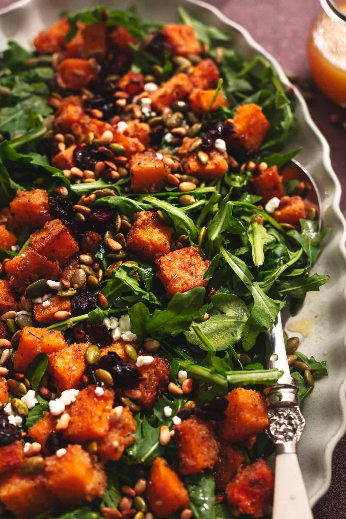 arugula salad on platter with roasted butternut squash, cranberries, and seeds