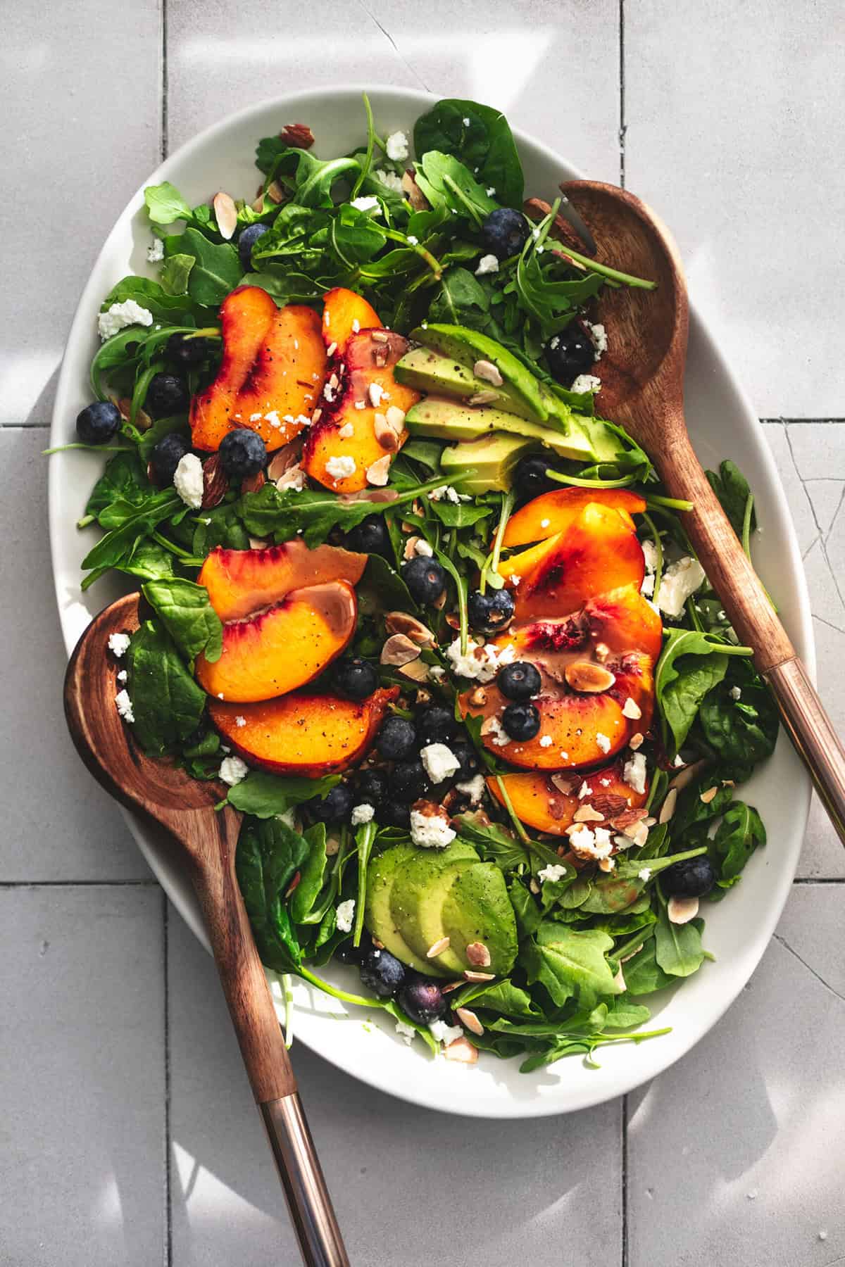 overhead view of platter with avocado peach and blueberry salad with wooden serving spoons