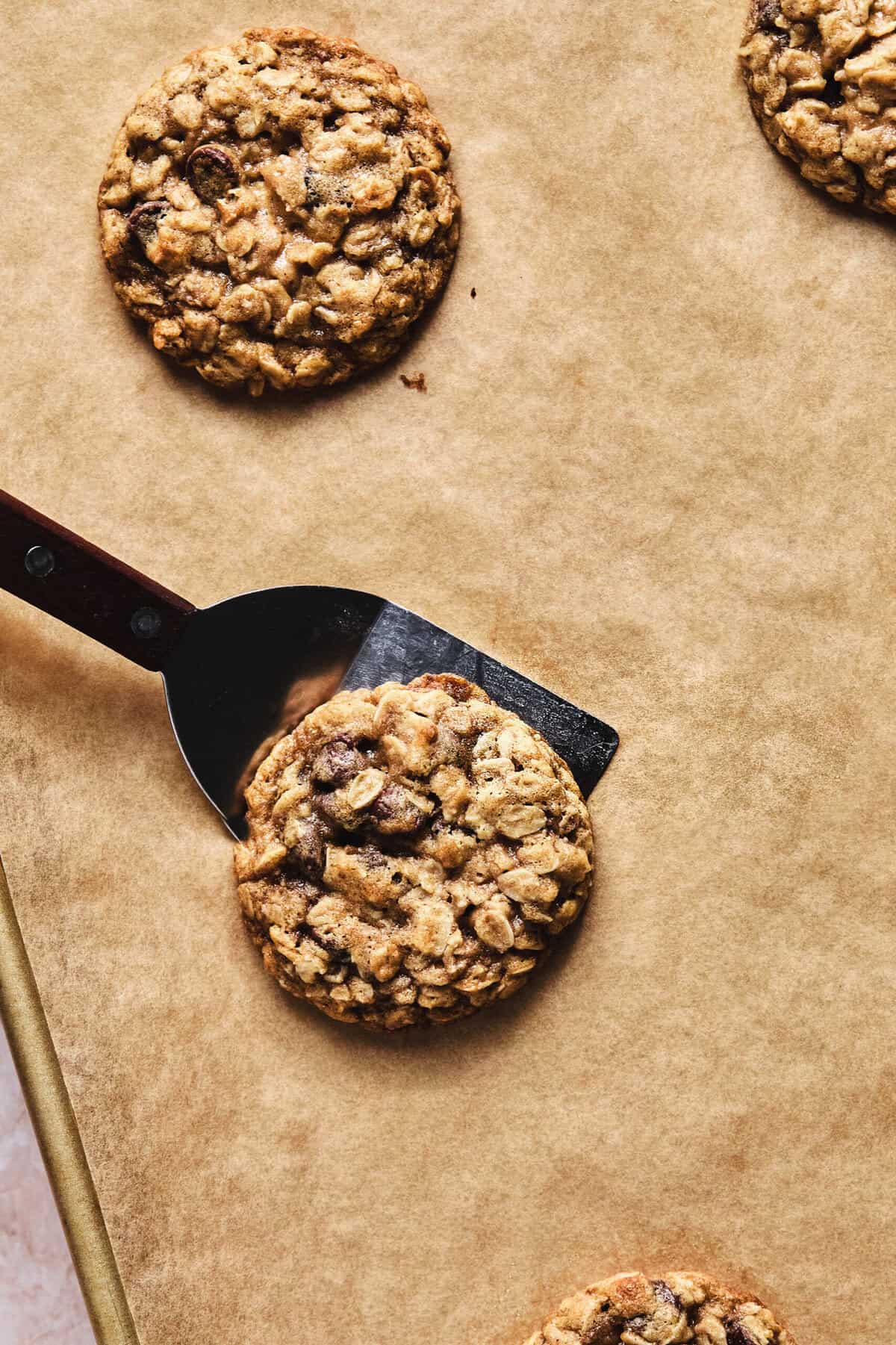 spatula lifting oatmeal cookie from pan lined with parchment