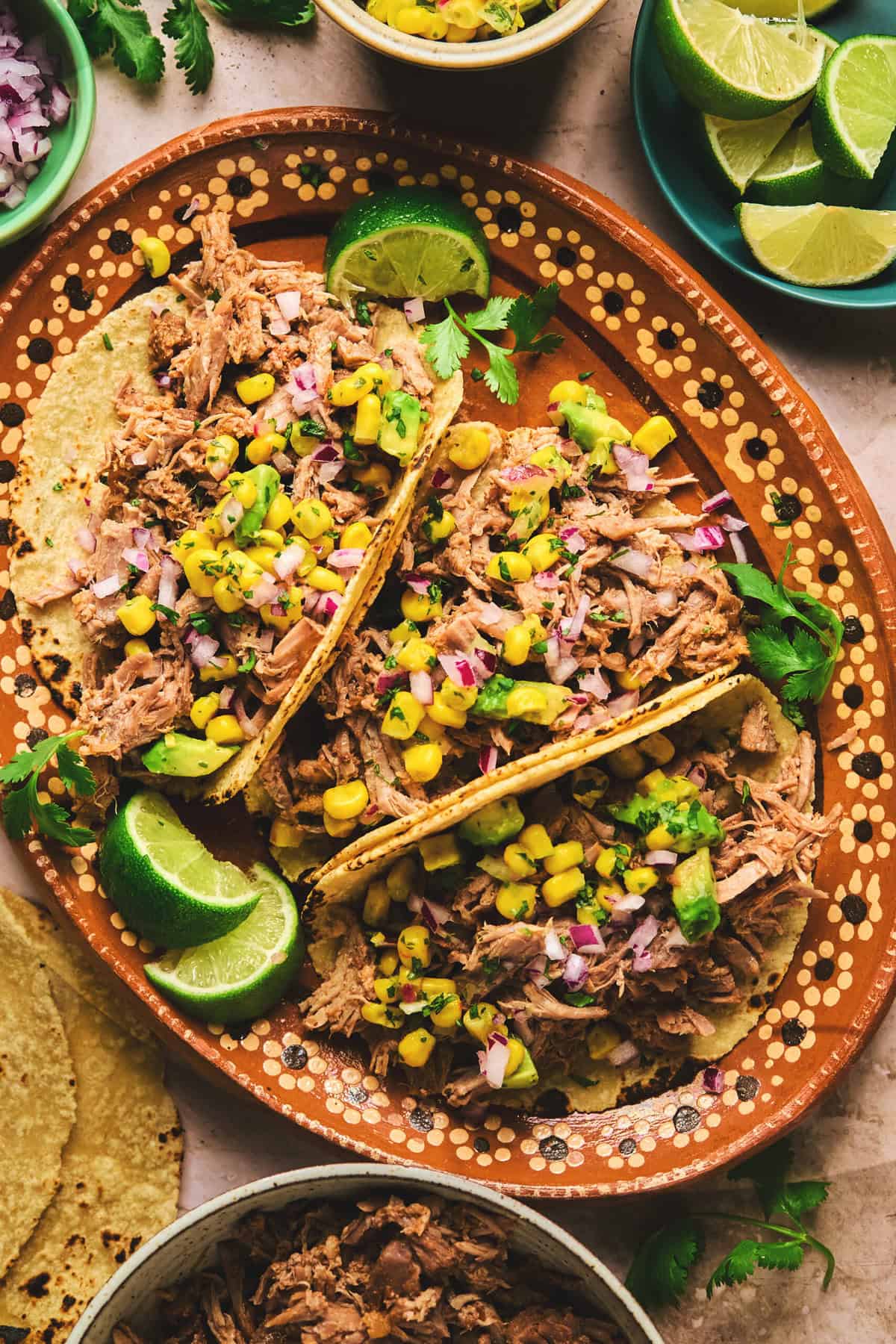 overhead view of three shredded pork tacos on a platter with lime wedges