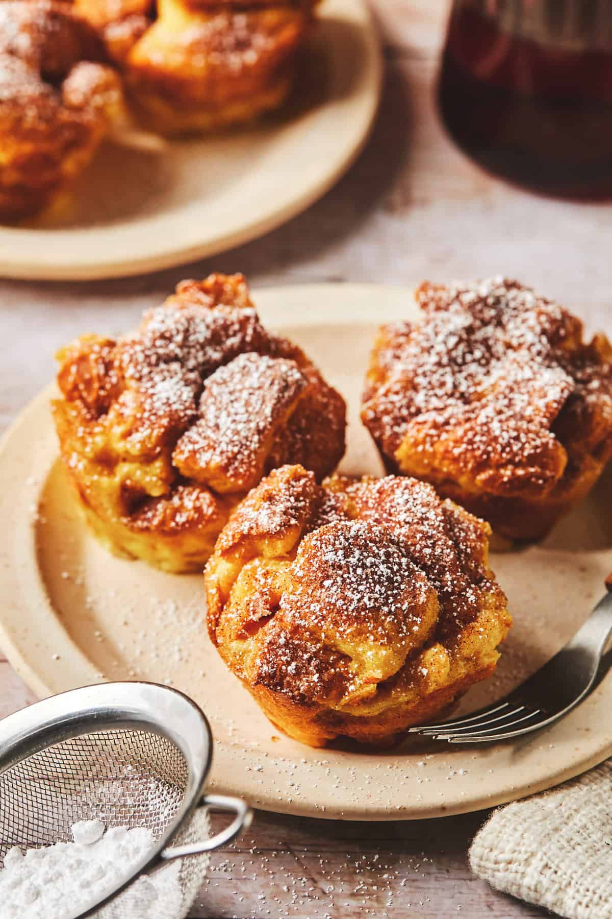 three french toasted muffins on a plate with powdered sugar on top