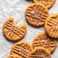 flourless peanut butter cookies on parchment paper with one cookie missing bite