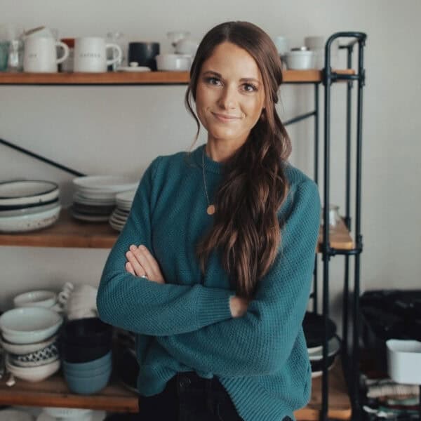 woman with folded arms standing in front of shelves of dishes