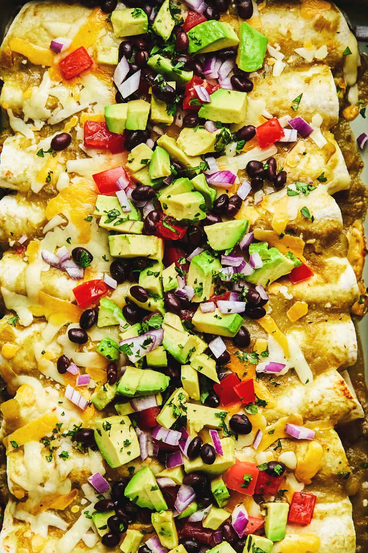 up close avocado, black beans, and tomatoes on top of enchiladas