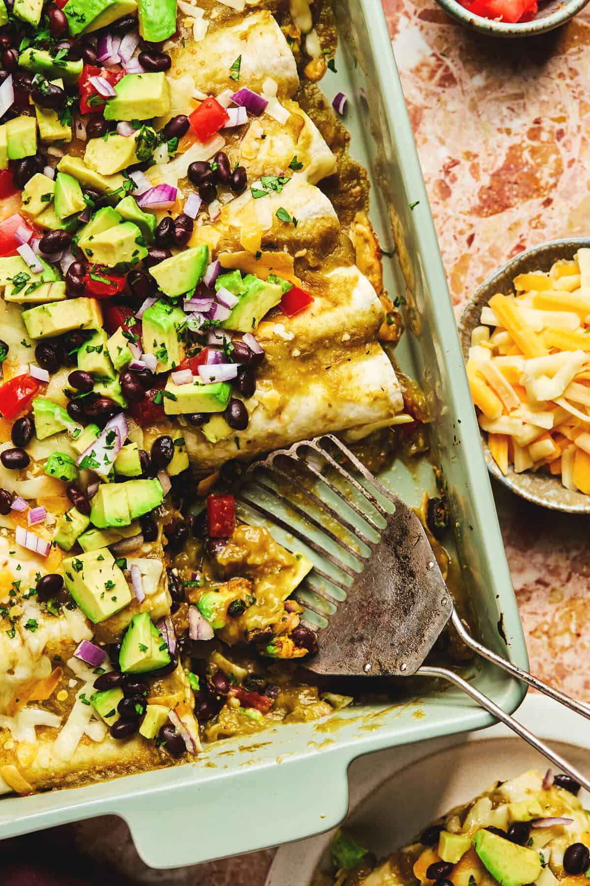 spatula dishing up black bean enchiladas from baking dish