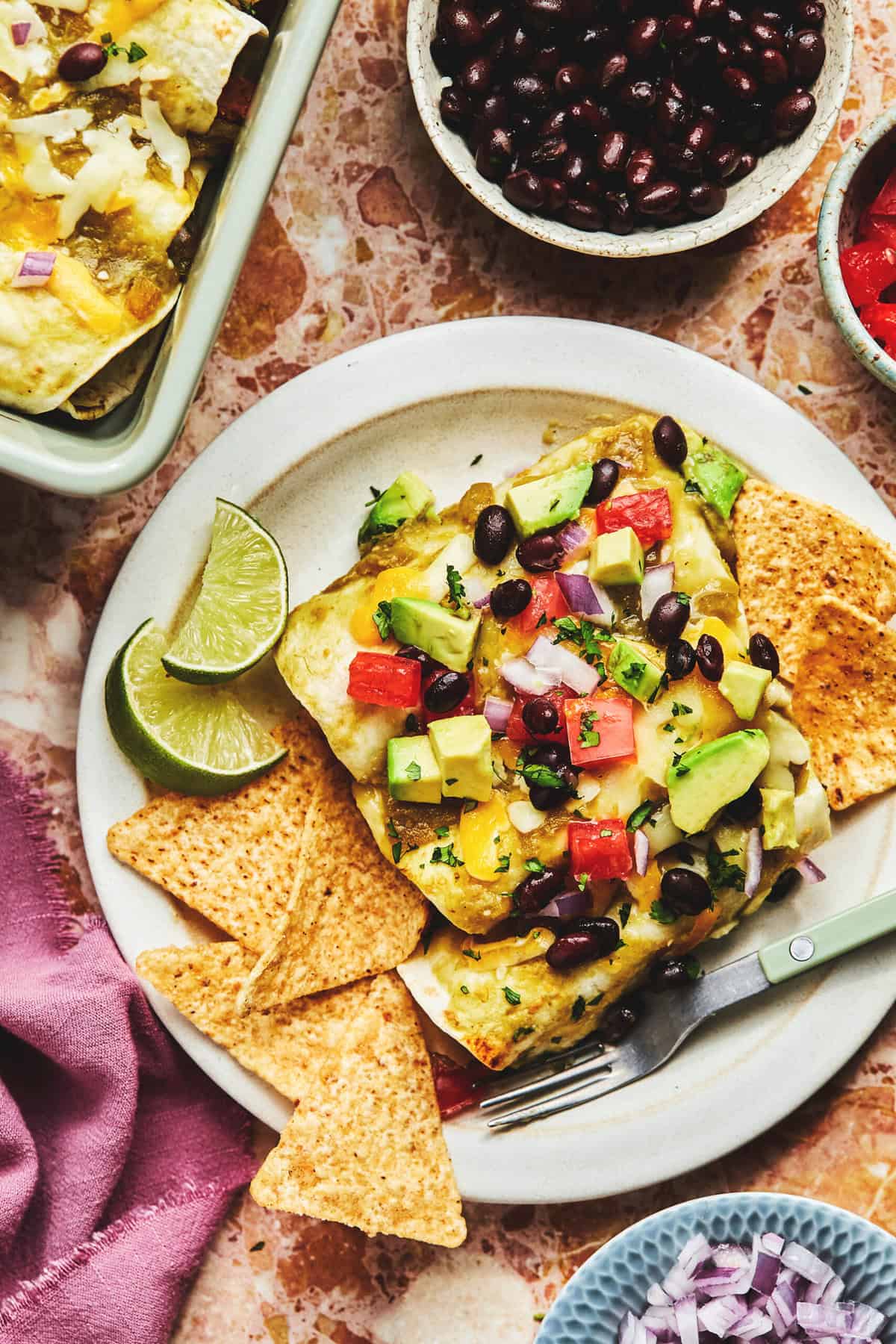 black bean vegetarian enchiladas with avocado and tomatoes on plate with chips and limes