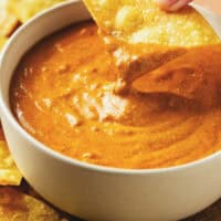 one chip dipping into queso cheese sauce in bowl