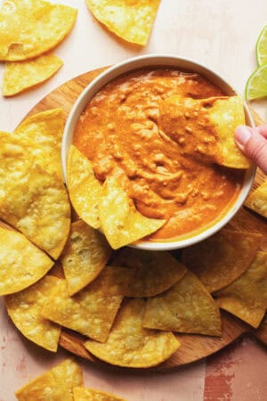 hand scooping chip into melted cheese dip in bowl surround by chips