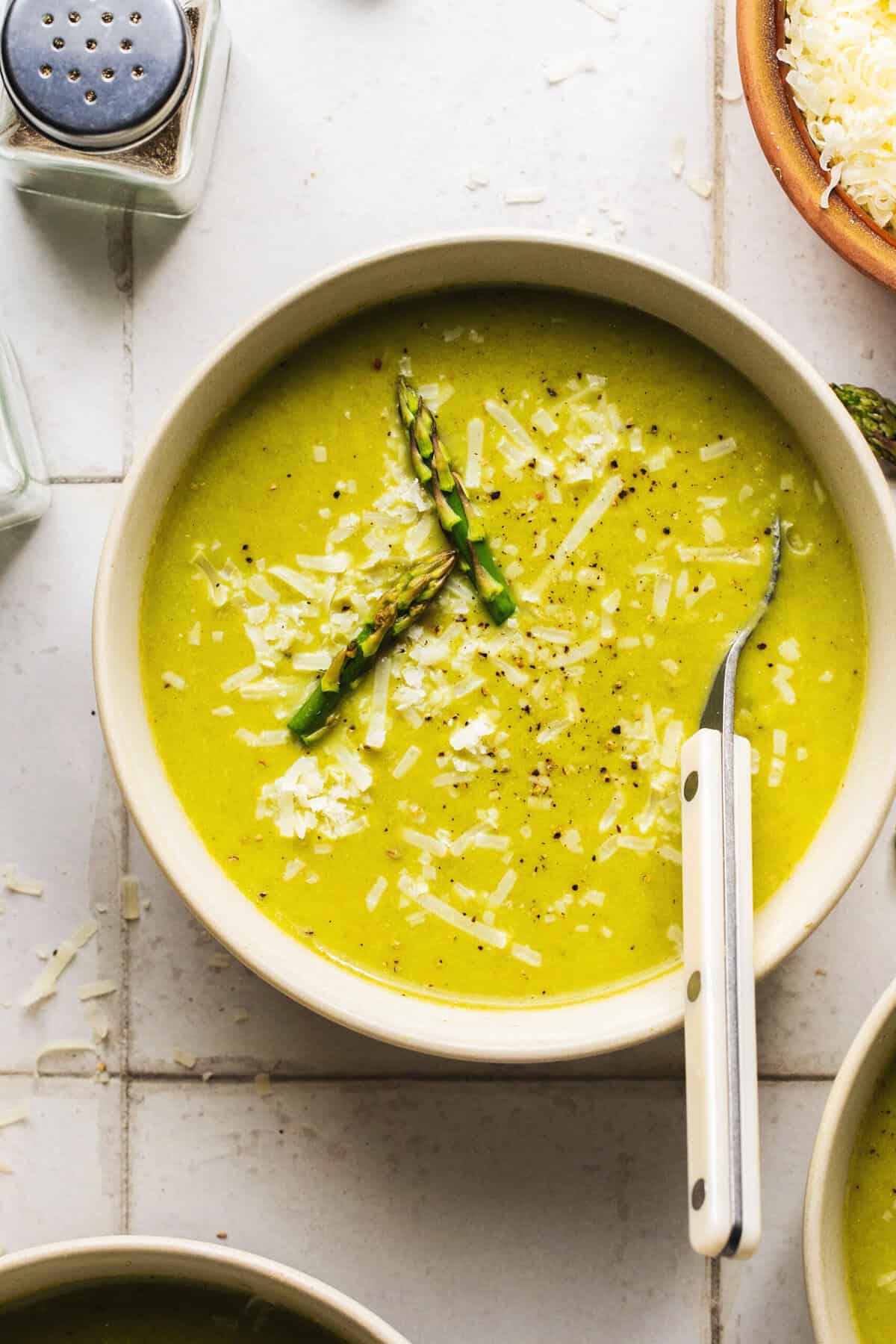 bowl of soup with whole asparagus pieces and parmesan cheese with spoon