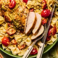 pesto chicken with tomatoes and pasta on plate with fork and knife