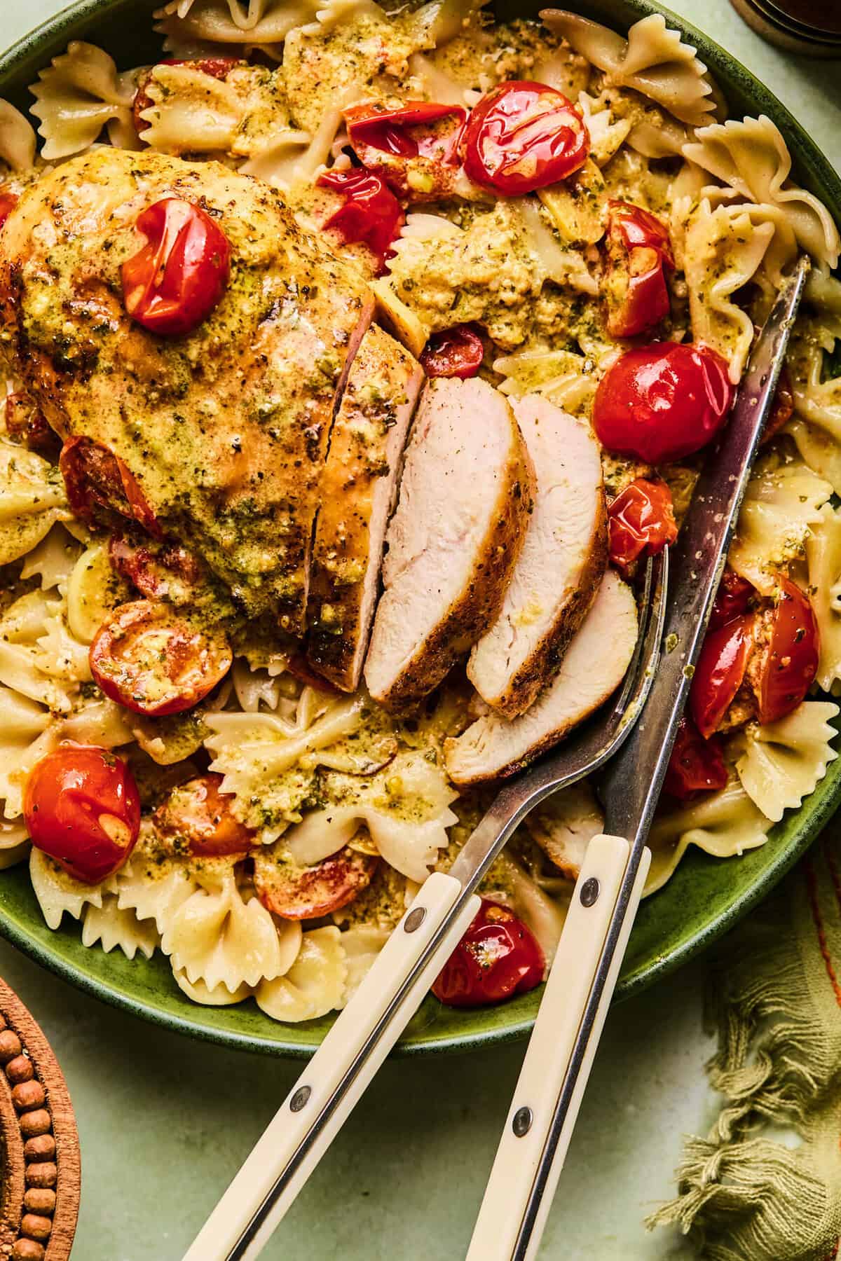 pesto chicken with tomatoes and pasta on plate with fork and knife