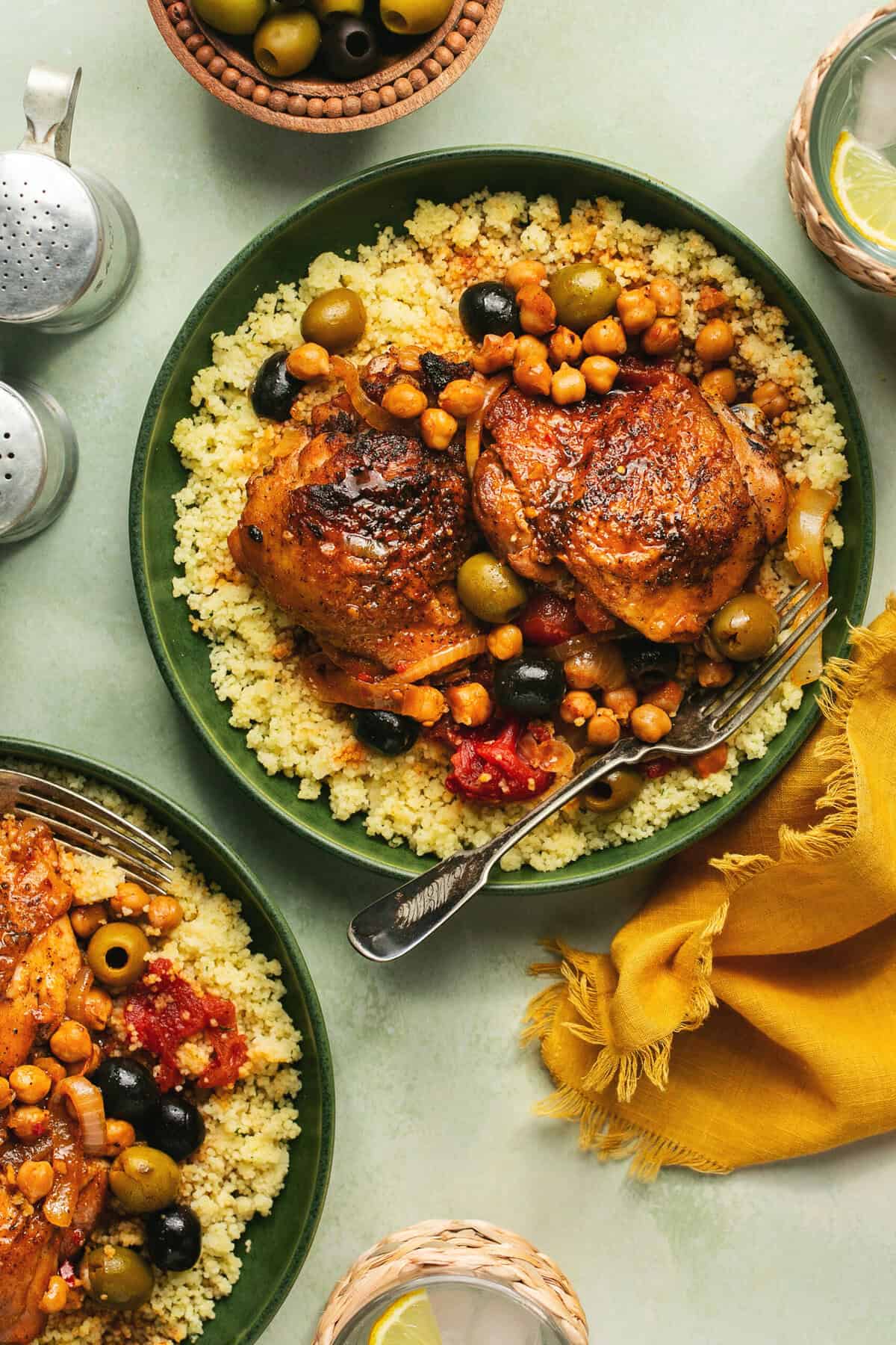 two plates of chicken thighs roasted with olives over couscous