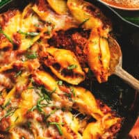 sausage stuffed pasta shells with fresh basil and meat sauce in skillet with spoon