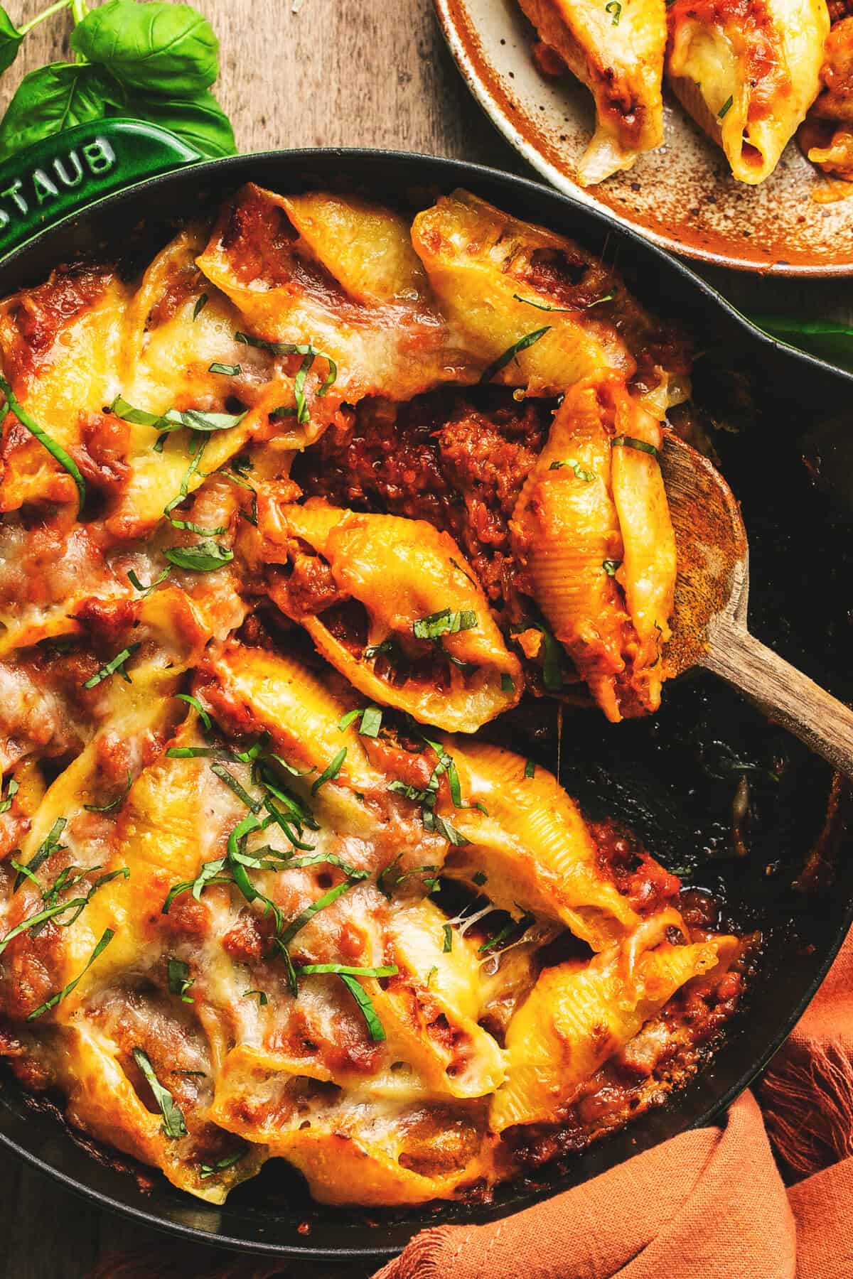 sausage stuffed pasta shells with fresh basil and meat sauce in skillet with spoon