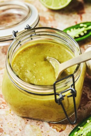 spoon dipping into green enchilada sauce in jar