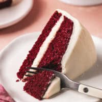 fork cutting into slice of layer cake with cream cheese frosting on plate