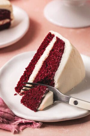 fork cutting into slice of layer cake with cream cheese frosting on plate