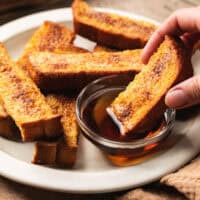 hand dipping french toast into syrup bowl