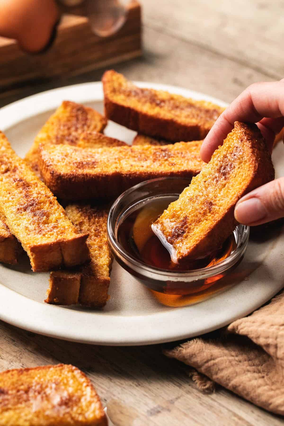 hand dipping french toast into syrup bowl